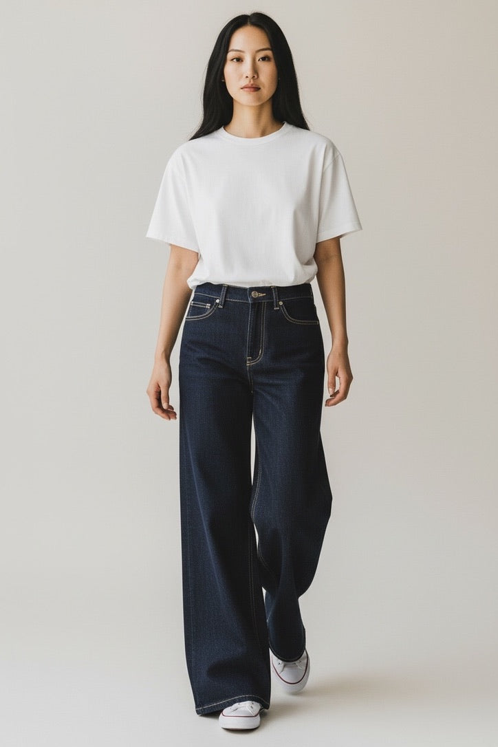 A woman modeling a white short-sleeve crewneck t-shirt and dark blue wide-leg jeans against a plain light gray studio background.